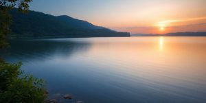 Calming sunset over a tranquil lake with greenery.